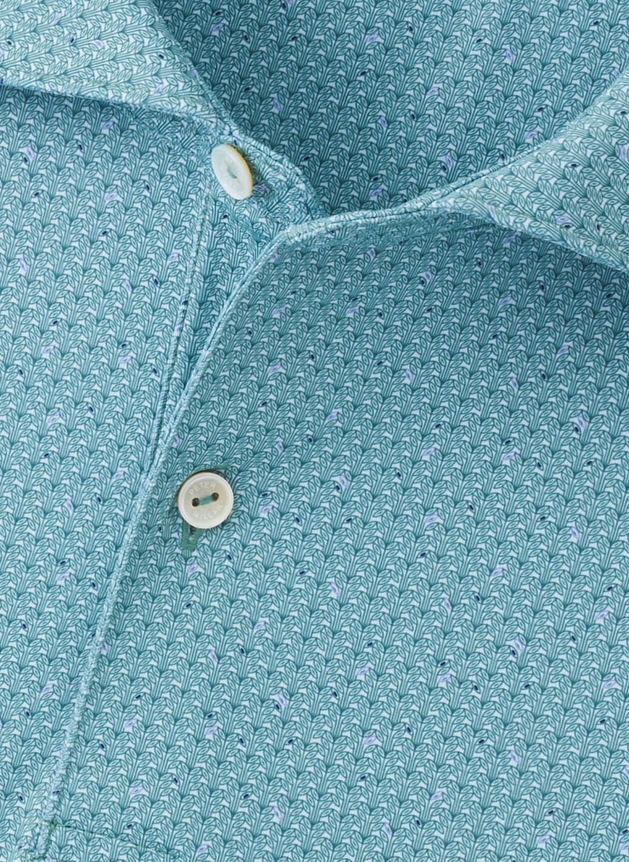 Close-up of the Peter Millar Corinth Performance Jersey Polo, a light blue shirt with a small leaf-like pattern, two white buttons, and four-way stretch for comfort.