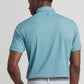 A man faces away, wearing the Peter Millar Corinth Performance Jersey Polo in light blue with UPF 50+ sun protection and light gray pants, set against a plain background.