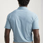 A man, seen from behind against a plain background, wears the Peter Millar Chase Performance Jersey Polo in light blue and navy stripes with four-way stretch, paired with beige pants.