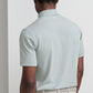 A man faces away from the camera, wearing a light gray Peter Millar Albatross Cotton-Blend Pique Polo, beige pants, and a textured beige belt against a plain light background.