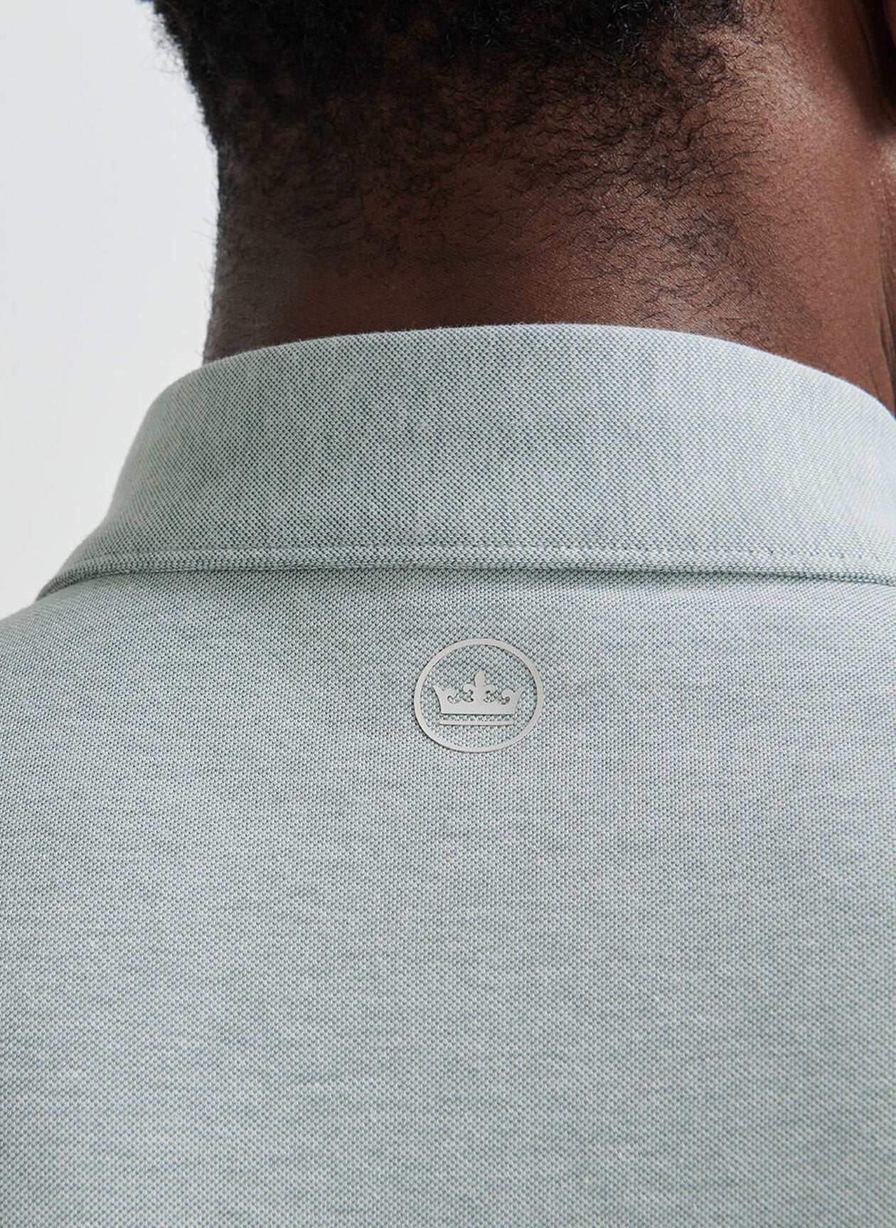 Close-up of the back of a person's neck and shoulders wearing the Peter Millar Albatross Cotton-Blend Pique Polo in light grey, featuring a small round logo at the top center.
