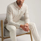 A man sits on a light gray chair wearing the Peter Millar Amble Long-Sleeve Cotton Cashmere Polo in beige, matching pants, and loafers, looking toward the camera.