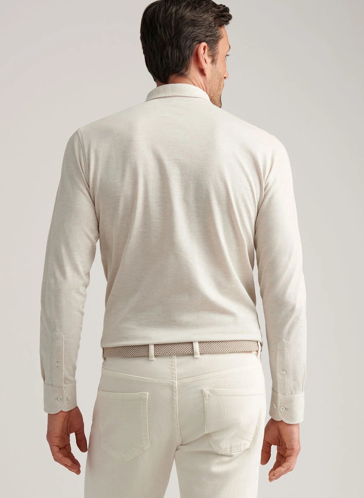 A man is shown from the back against a plain background wearing the Peter Millar Amble Long-Sleeve Cotton Cashmere Polo in light beige with matching pants, adding a refined touch to his understated look.