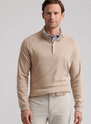 A man stands facing the camera against a plain background, wearing the Peter Millar Grant Birdseye Quarter-Zip sweater over a collared shirt and light-colored pants.