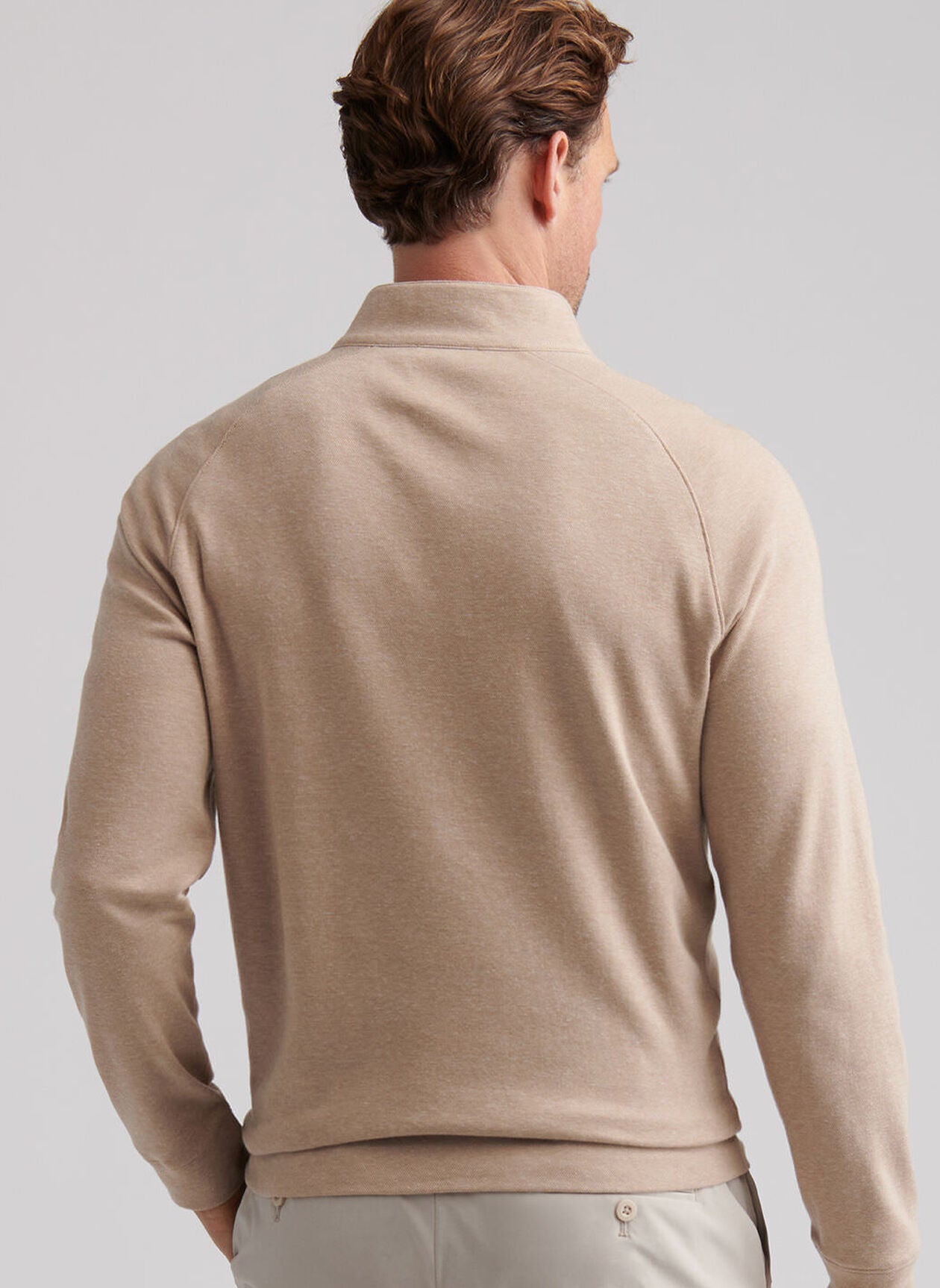 A man is seen from behind wearing the Peter Millar Grant Birdseye Quarter-Zip, a light beige long-sleeve top, paired with light pants, standing against a plain background.