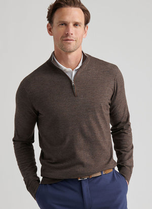 Man wearing a brown Peter Millar Excursionist Flex Quarter-Zip Sweater over a white collared shirt and blue pants, standing with hands in pockets against a plain background.