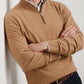 A man stands with his arms crossed over a collared shirt, wearing the Peter Millar Artisan Crafted Cashmere Flex Quarter-Zip in tan, inspired by classic British Isles knit styles.