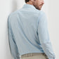 A man stands with his back to the camera, looking over his shoulder, wearing the Peter Millar Bechet Performance Poplin Sport Shirt in light blue checks and beige pants.