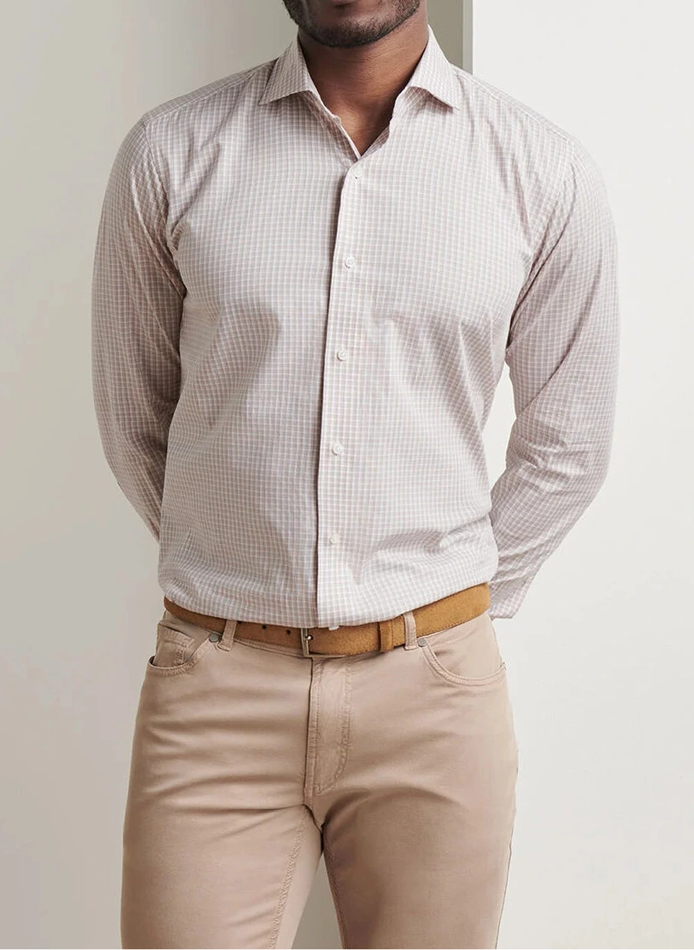 A man stands against a white background wearing a Peter Millar Torino Cotton Sport Shirt in a light checkered pattern, paired with beige pants and a tan belt.