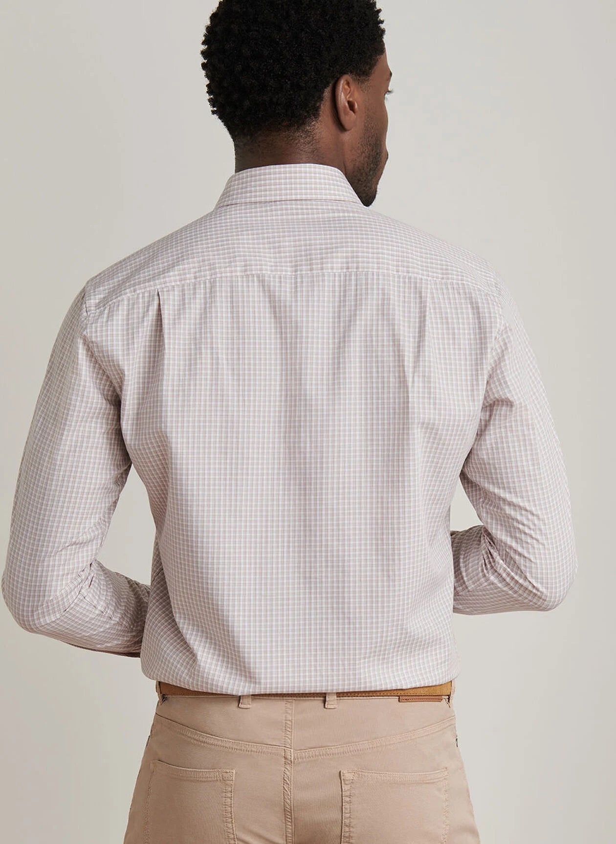 A man faces away from the camera, wearing the Peter Millar Torino Cotton Sport Shirt featuring light plaid stretch cotton with a Flex Finish, paired with beige pants.