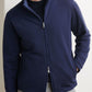 A man wears the Peter Millar Ryder Reversible Jacket in navy over a black shirt and light gray pants, standing with one hand in his pocket.