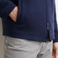 A person wearing a Peter Millar Ryder Reversible Jacket in navy blue with one hand in the jacket pocket, paired with light gray pants.