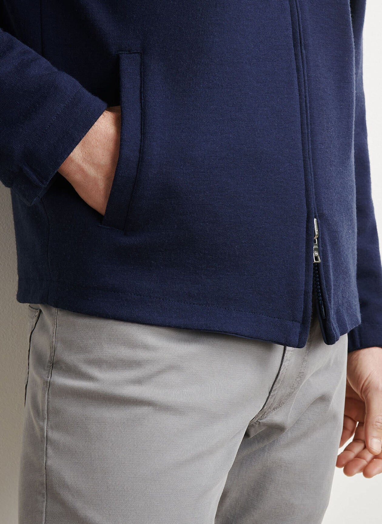 A person wearing a Peter Millar Ryder Reversible Jacket in navy blue with one hand in the jacket pocket, paired with light gray pants.