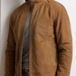 A man wears the Peter Millar Soho Suede Bomber, a lightweight jacket with a microfiber lining, over a grey shirt against a plain light-colored background.