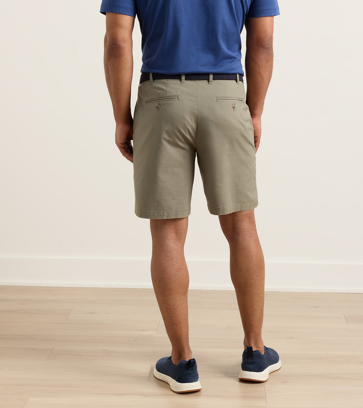 Back view of a person wearing Crown Comfort Short 8″ inseam khaki shorts, a blue polo shirt, and navy sneakers, showcasing a clean, plain weave fabric.
