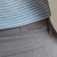 Close-up of a person wearing a light blue striped shirt tucked into gray Peter Millar eb66 Melange Performance Five-Pocket Pants, crafted in stretch twill fabric for all-day comfort.