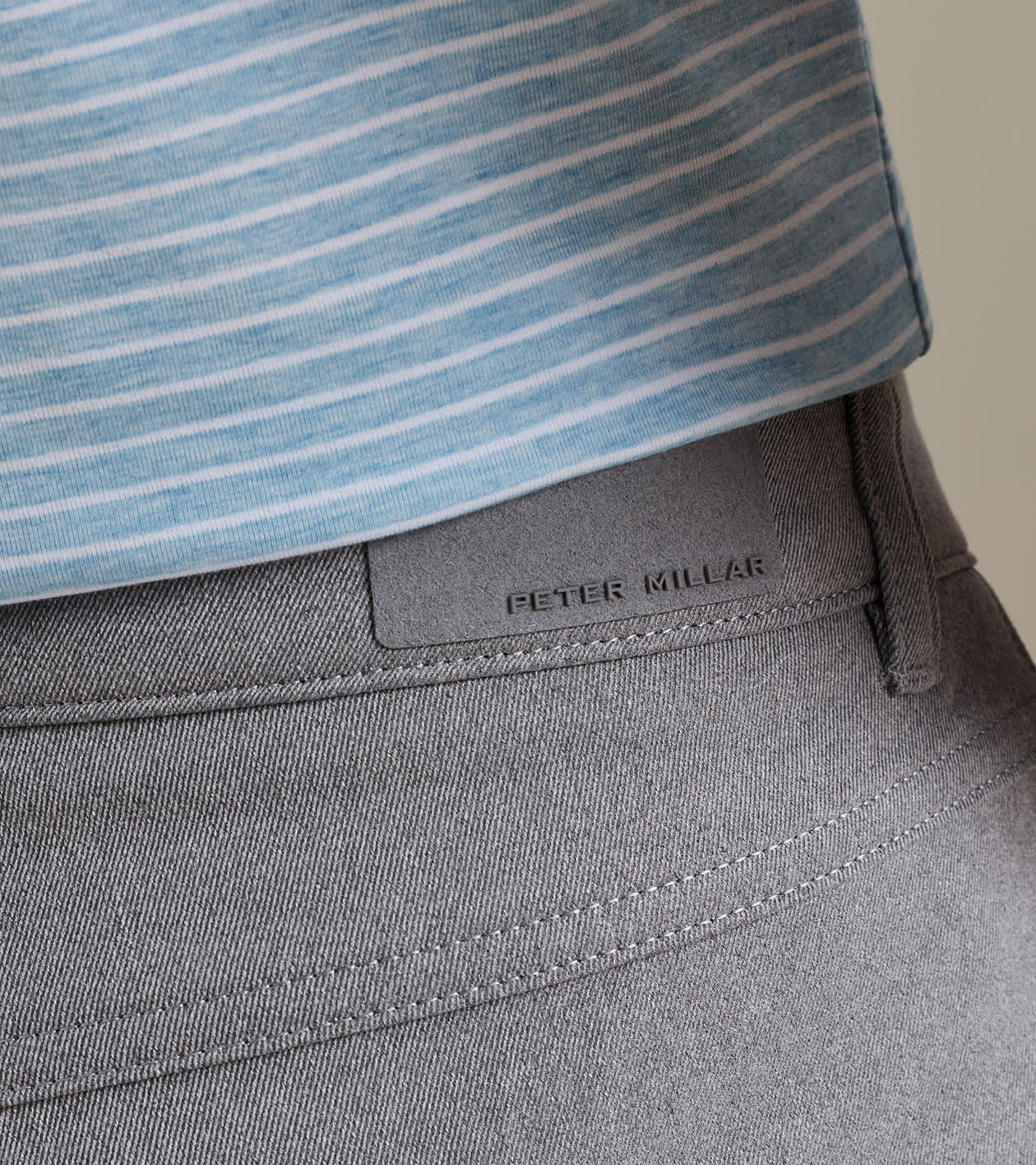 Close-up of a person wearing a light blue striped shirt tucked into gray Peter Millar eb66 Melange Performance Five-Pocket Pants, crafted in stretch twill fabric for all-day comfort.