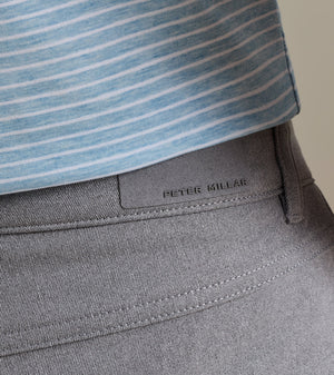 Close-up of a person wearing a light blue striped shirt tucked into gray Peter Millar eb66 Melange Performance Five-Pocket Pants, crafted in stretch twill fabric for all-day comfort.