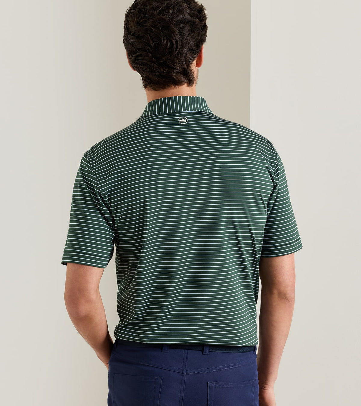 Back view of a person wearing a green and white striped Peter Millar Oaks Performance Jersey Polo with a small circular logo at the base of the collar.
