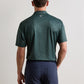 Back view of a person wearing a dark green, four-way stretch patterned Transfusion Performance Jersey Polo and navy blue trousers.
