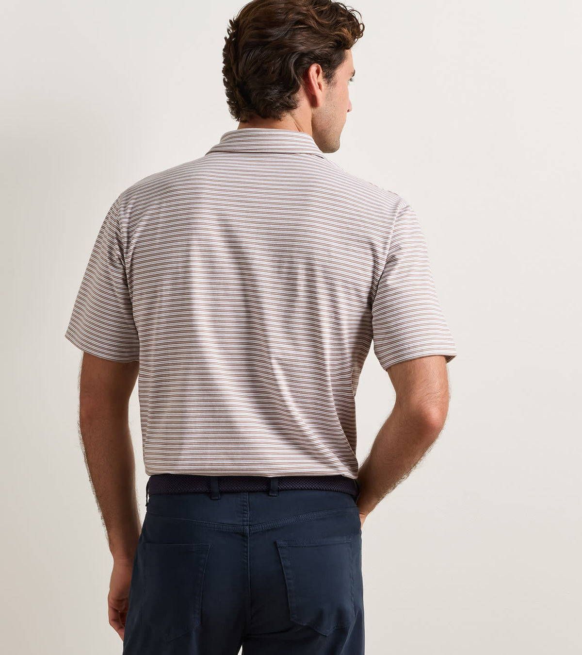 Back view of a person wearing a brown and white striped Turner Crown Flex Cotton Polo and dark pants, crafted from jersey-knit cotton for all-day comfort.