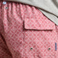 Close-up of a person wearing the Peter Millar Tails of Summer Swim Trunk, featuring a pink patterned design with a flap pocket and visible brand tag, an elastic drawstring waistband, paired with a light gray shirt.