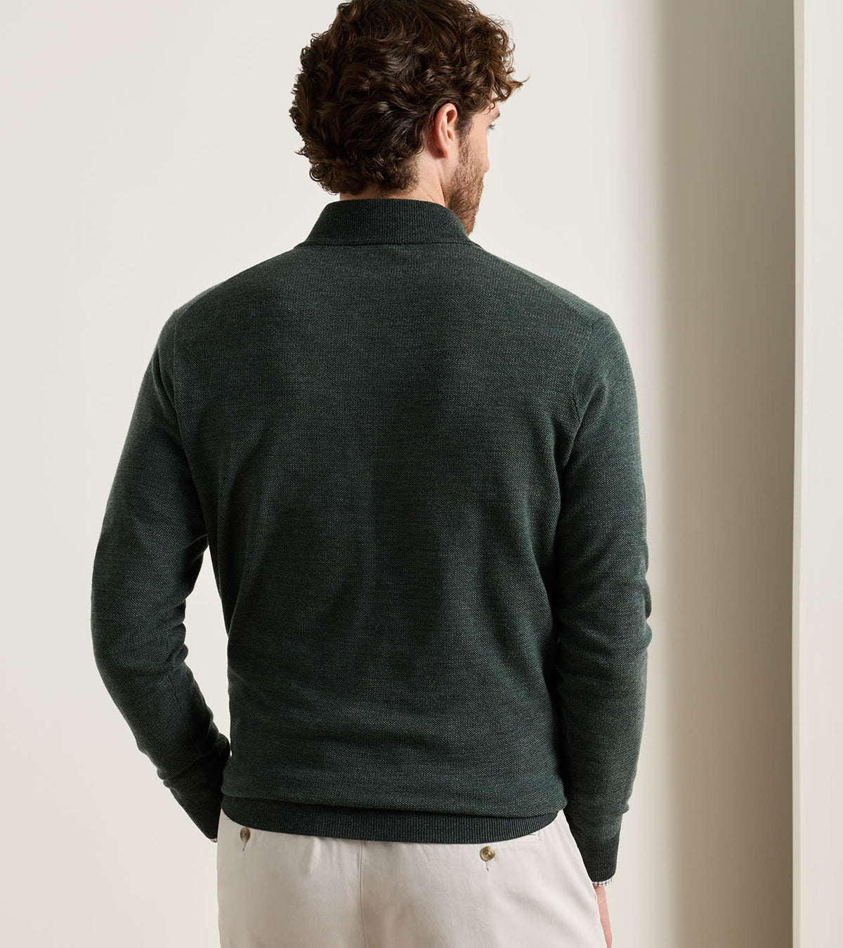 Back view of a person wearing a dark green Blair Birdseye Quarter-Zip Sweater and light-colored trousers.