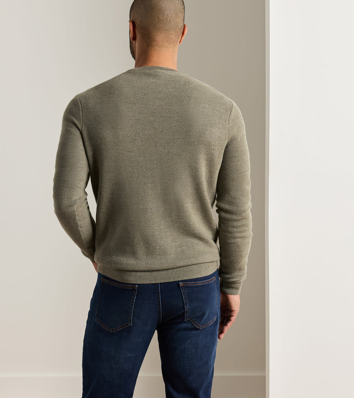 Back view of a person wearing a sage green 12 gauge Autumn Crest Honeycomb Crewneck Sweater and dark blue jeans.