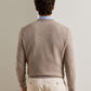 A person seen from behind wears a tan Peter Millar Autumn Crest Honeycomb Crewneck Sweater over a light blue collared shirt and cream trousers.
