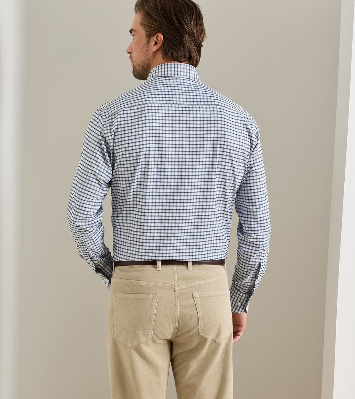 A man seen from behind wearing a blue and white grid-patterned Peter Millar Charles Performance Twill Sport Shirt tucked into tan trousers.