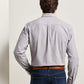 A man stands with his back to the camera, wearing the Peter Millar Devonport Chambray Cotton-Stretch Sport Shirt in light gray, tucked into blue jeans and paired with a brown belt for a relaxed casual style.