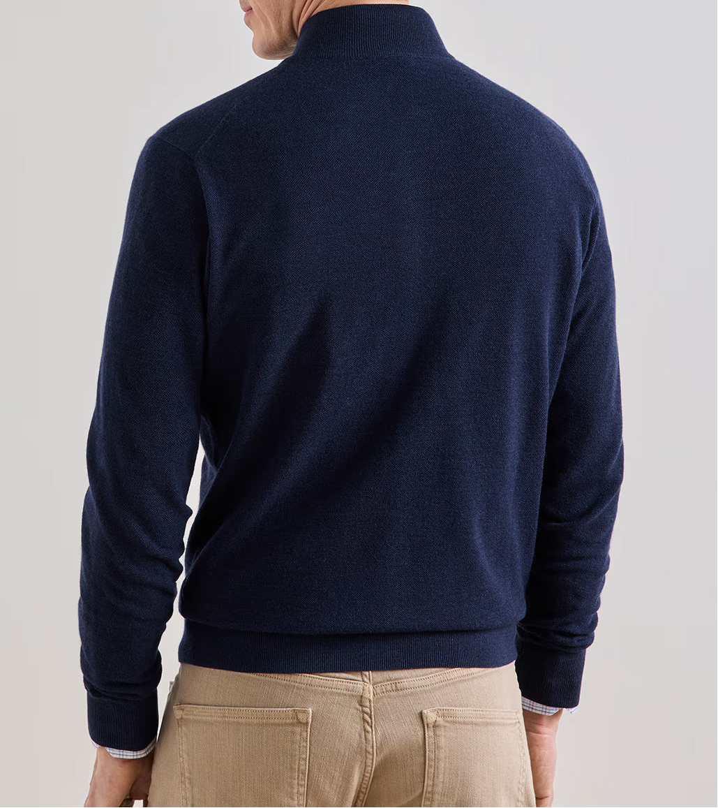 A person viewed from the back, wearing a navy blue Peter Millar Excursionist Flex Full Zip Sweater and tan trousers.
