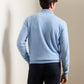 A man stands with his back to the camera, wearing the Peter Millar Artisan Crafted Cashmere Flex Quarter-Zip in light blue and dark pants, in a softly lit indoor setting.