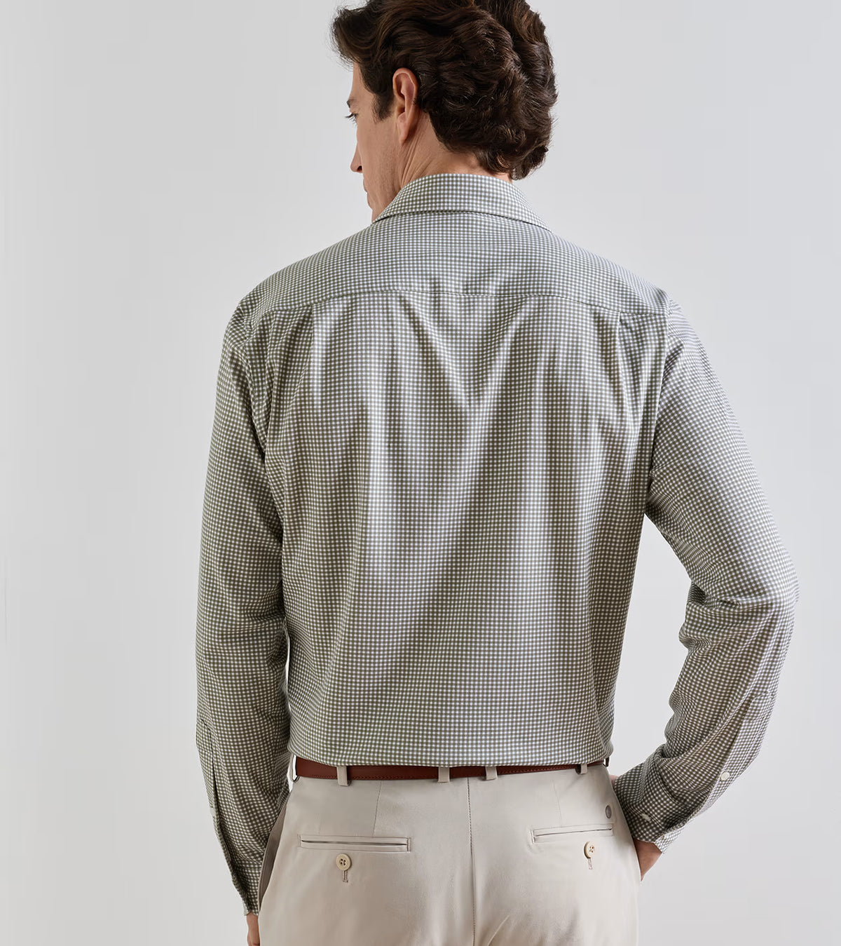 Back view of a man wearing an olive and white Peter Millar Excursionist Flex Gingham Sport Shirt tucked into light-colored trousers with a brown belt.
