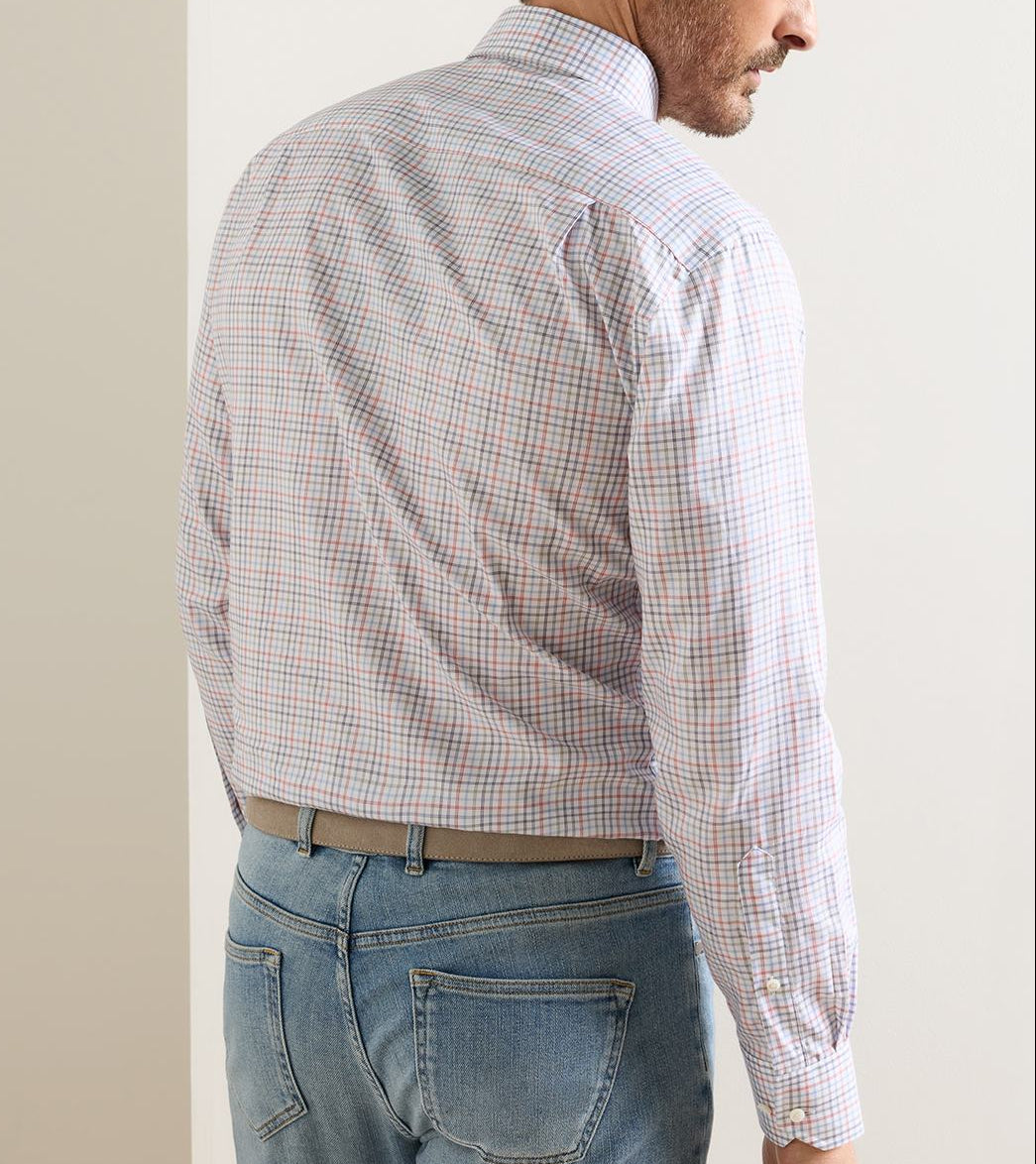 A man wears a Peter Millar Otis Cotton Sport Shirt, featuring a multicolored grid pattern on white cotton poplin, tucked into light-wash blue jeans with a tan belt.