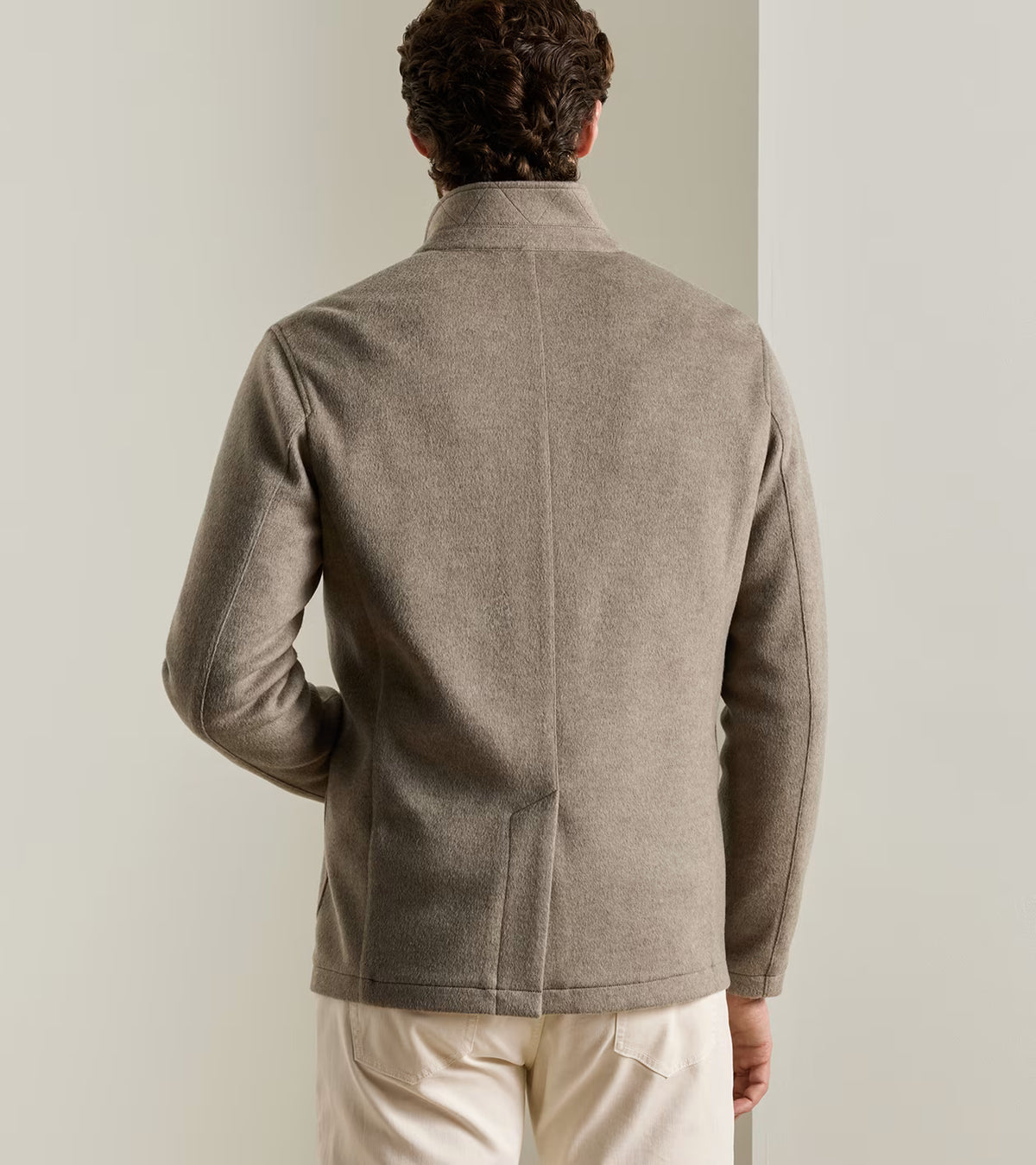 Back view of a man wearing a tan Peter Millar Crown Flex Merino blazer with a stand collar.