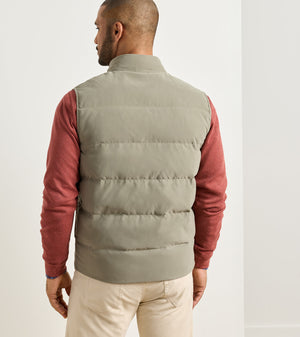 A man seen from behind wearing an olive Bedford Quilted Vest over a red long-sleeve shirt and tan pants.