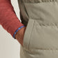 Close-up of a person wearing a light olive Bedford Quilted Vest by Peter Millar over a red long-sleeved shirt, with a hand tucked into the pocket.