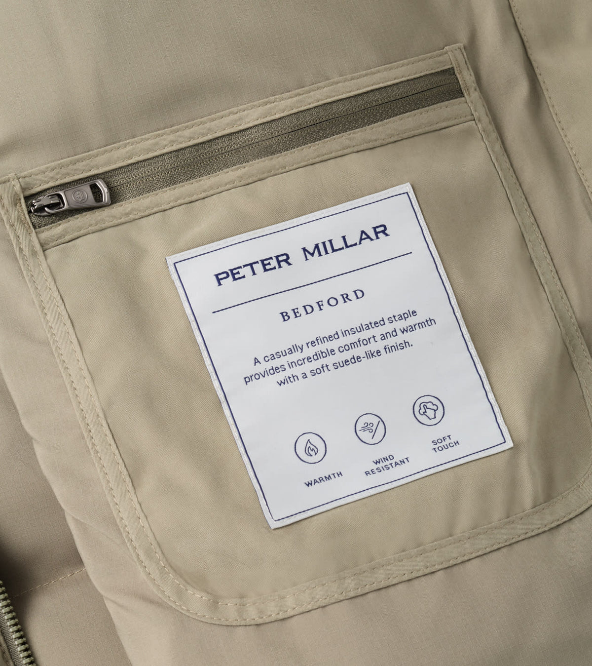 Peter Millar Bedford Quilted Vest in tan with midweight insulation, featuring a zippered pocket and a rectangular interior label detailing its warmth, wind resistance, and soft touch.