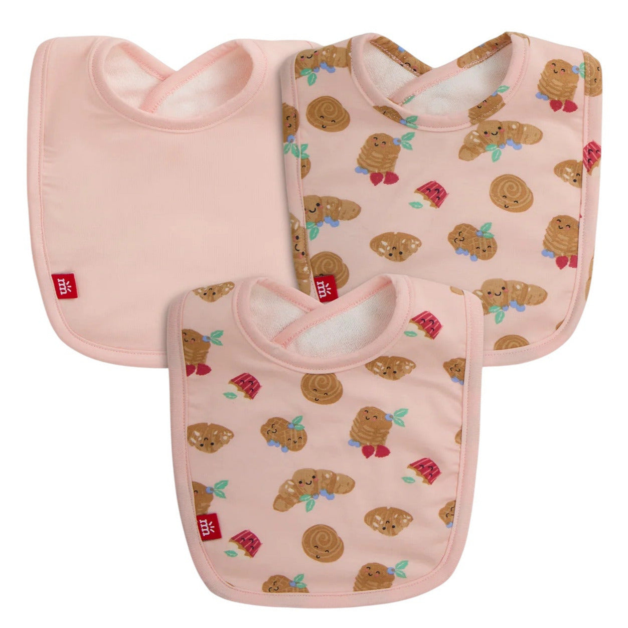 The Magnetic Me Bake My Day Modal Bib 3-Pack includes three eco-friendly pink bibs: two with cinnamon roll and cookie prints and one solid pink, each finished with a red logo tag.