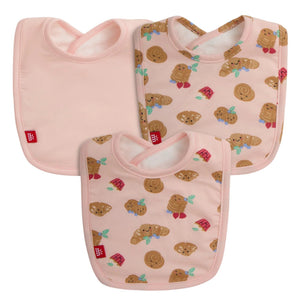 The Magnetic Me Bake My Day Modal Bib 3-Pack includes three eco-friendly pink bibs: two with cinnamon roll and cookie prints and one solid pink, each finished with a red logo tag.