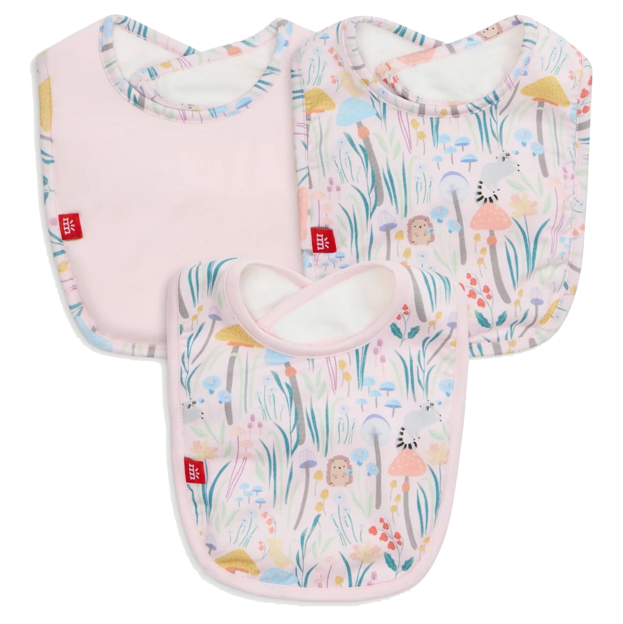 The Magnetic Me Shroom and Bloom Modal Bib 3-Pack includes three bibs: one solid pink and two with pastel floral and animal prints, all featuring rounded edges and a small red tag on the side.