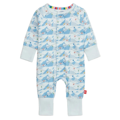 The Magnetic Me Baby Apres Chic Modal Convertible Coverall features a light blue mountain and skier pattern, sustainable modal fabric, light blue cuffs, multicolor stripe collar lining, and easy magnetic closures.