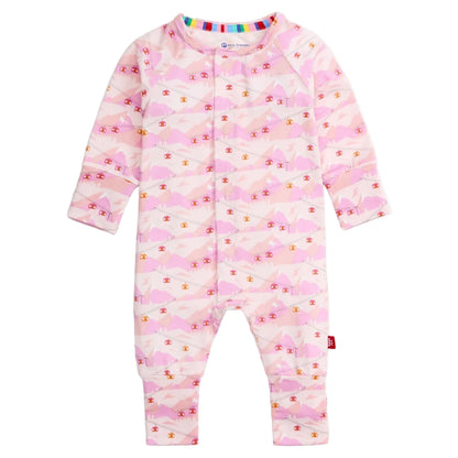 The Magnetic Me Baby Apres Chic Modal Convertible Coverall is a pink long-sleeve onesie with a mountain and cottage pattern, front snap closures, and rainbow-trimmed collar.