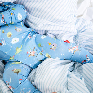 A child in the Magnetic Me Baby Boys' Good Knight Modal Convertible Coverall lies on a bed with blue and white striped sheets and pillow.