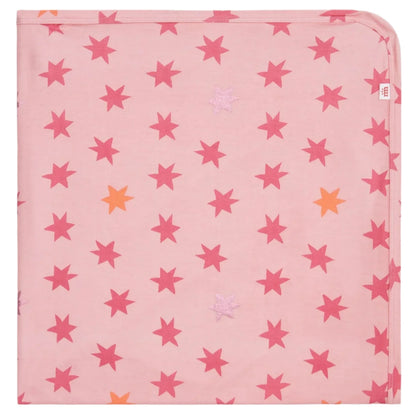 The Cosmic Confetti Baby Blanket by Magnetic Me is a pink square stroller blanket with red, orange, and light pink stars, one rounded corner, and a white tag—made from temperature-regulating fabric for your baby’s comfort.