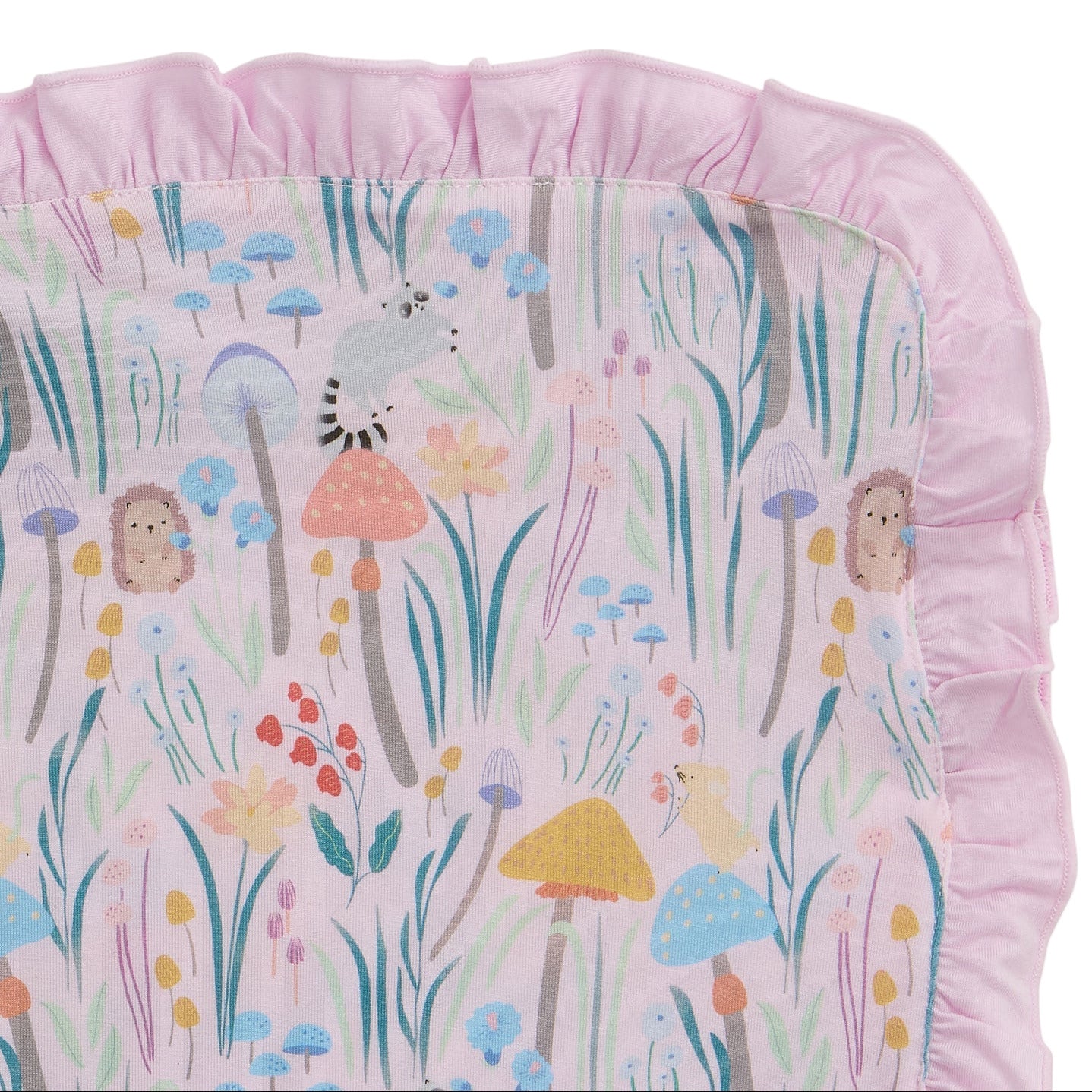The Magnetic Me Shroom and Bloom Modal Blanket with Ruffles is a rectangular pink blanket with ruffled edges, decorated in a whimsical woodland print of hedgehogs, lemurs, mushrooms, and flowers in soft pastel hues. Perfect for babies!.