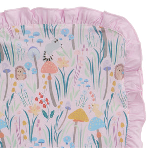 The Magnetic Me Shroom and Bloom Modal Blanket with Ruffles is a rectangular pink blanket with ruffled edges, decorated in a whimsical woodland print of hedgehogs, lemurs, mushrooms, and flowers in soft pastel hues. Perfect for babies!.
