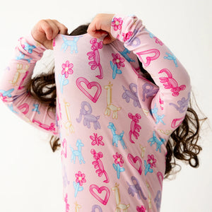 A child pulls the Baby and Kids' Party Animals Glow in the Dark Modal Magnetic PJ Set by Magnetic Me over their head, face partially covered—colorful animal and heart prints make bedtime dressing fun and easy.