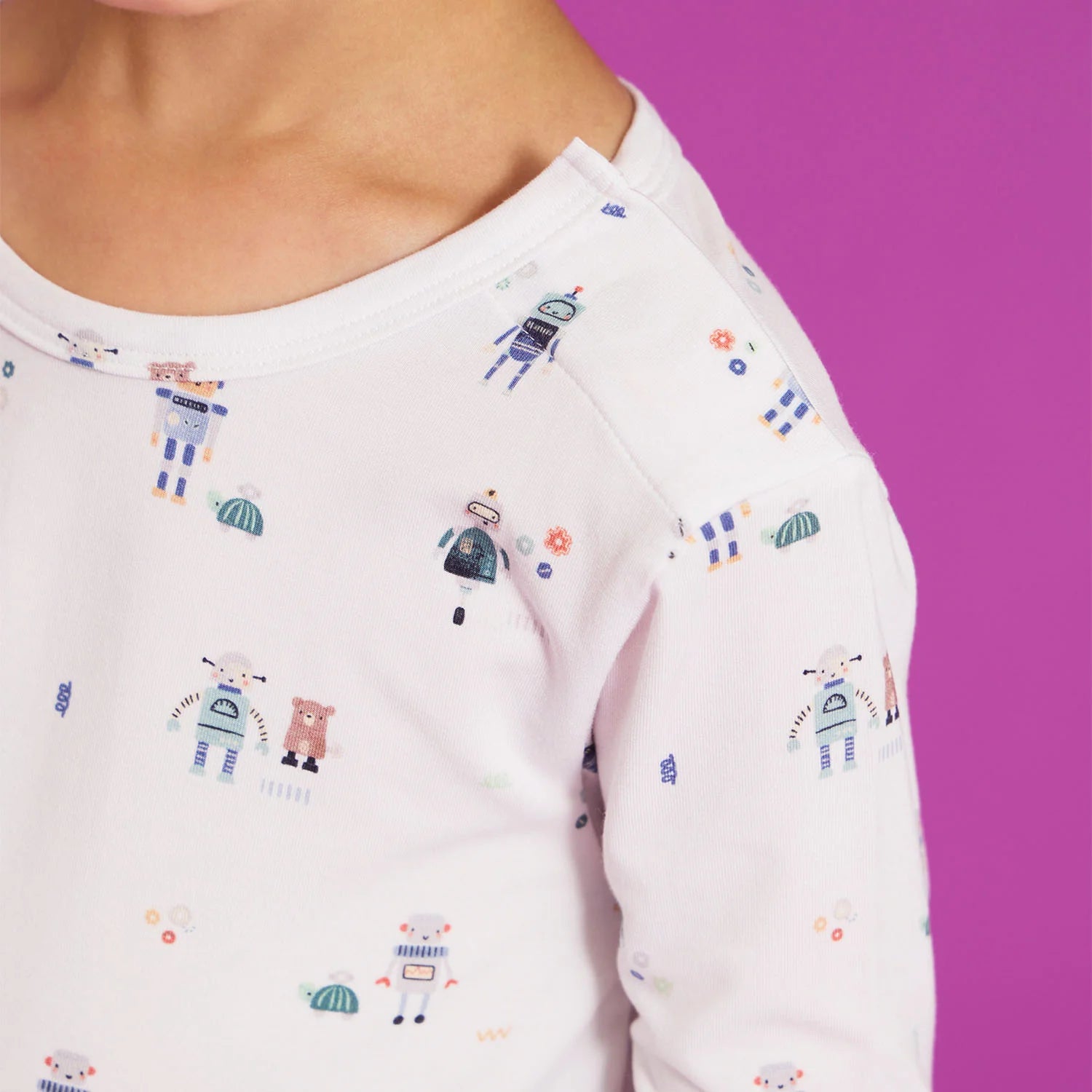 A child wears the Magnetic Me Baby Boys' and Boys' Love You a Bot Modal PJ Set, featuring light-colored fabric with robot and animal prints, standing against a purple background.